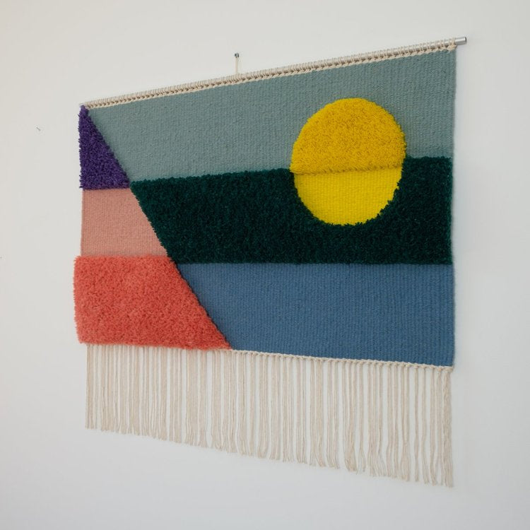 Opera tessile contemporanea tessuta a mano da Ilary Bottini, paesaggio astratto con toni di azzurro, blu, verde, rosa, viola e giallo con campiture geometriche orizzontali, diagonali e circolari a alternanza di sezioni tessute e annodate