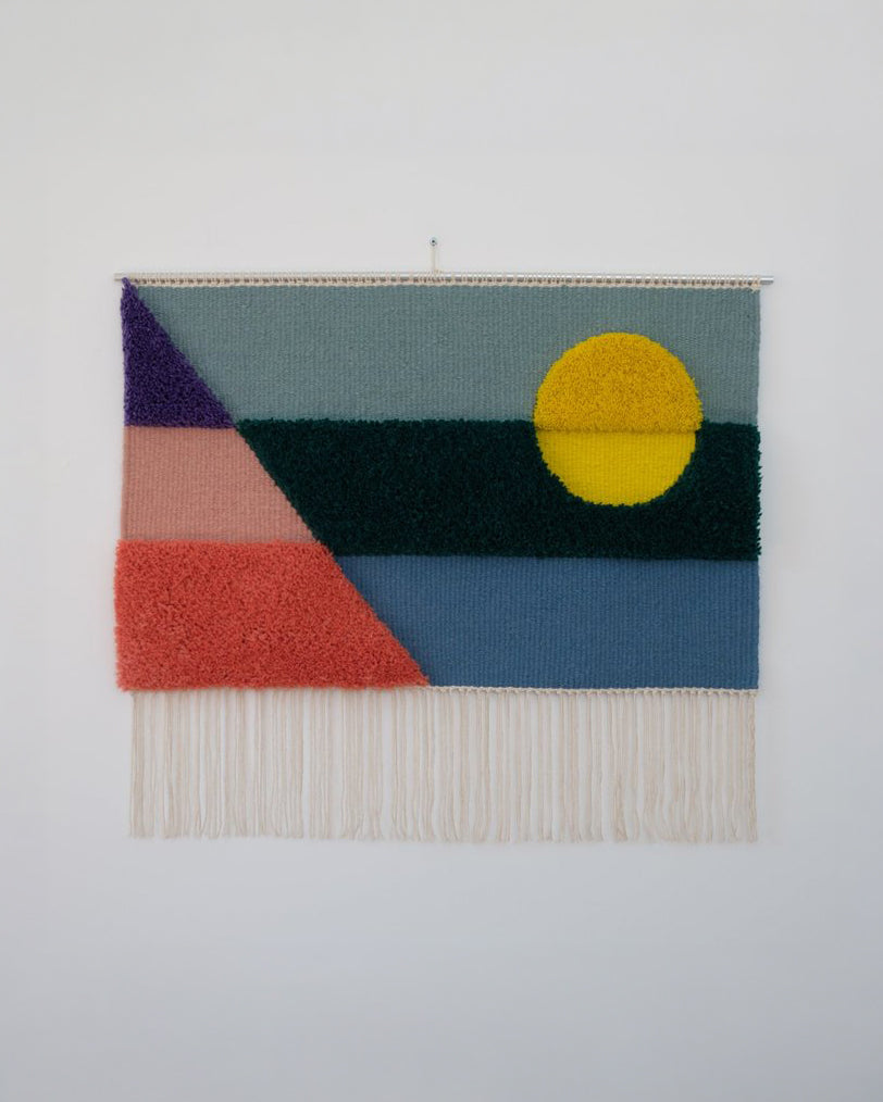 Opera tessile contemporanea tessuta a mano da Ilary Bottini, paesaggio astratto con toni di azzurro, blu, verde, rosa, viola e giallo con campiture geometriche orizzontali, diagonali e circolari a alternanza di sezioni tessute e annodate