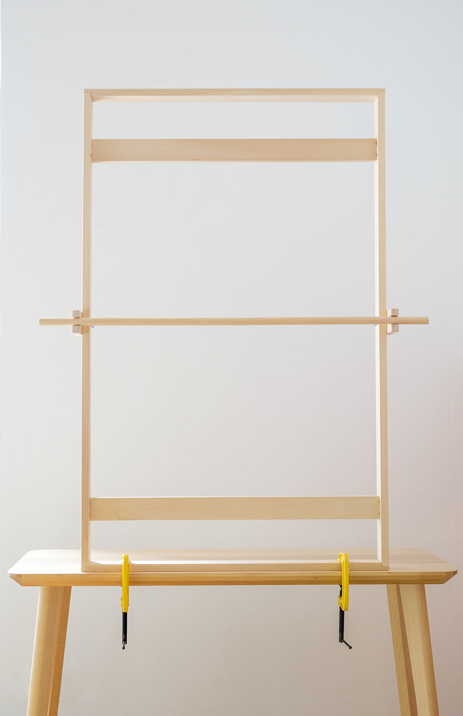 Telaio verticale in legno massello per tessitura di tappeti e arazzi, fissato su un tavolo in legno con morsetti gialli