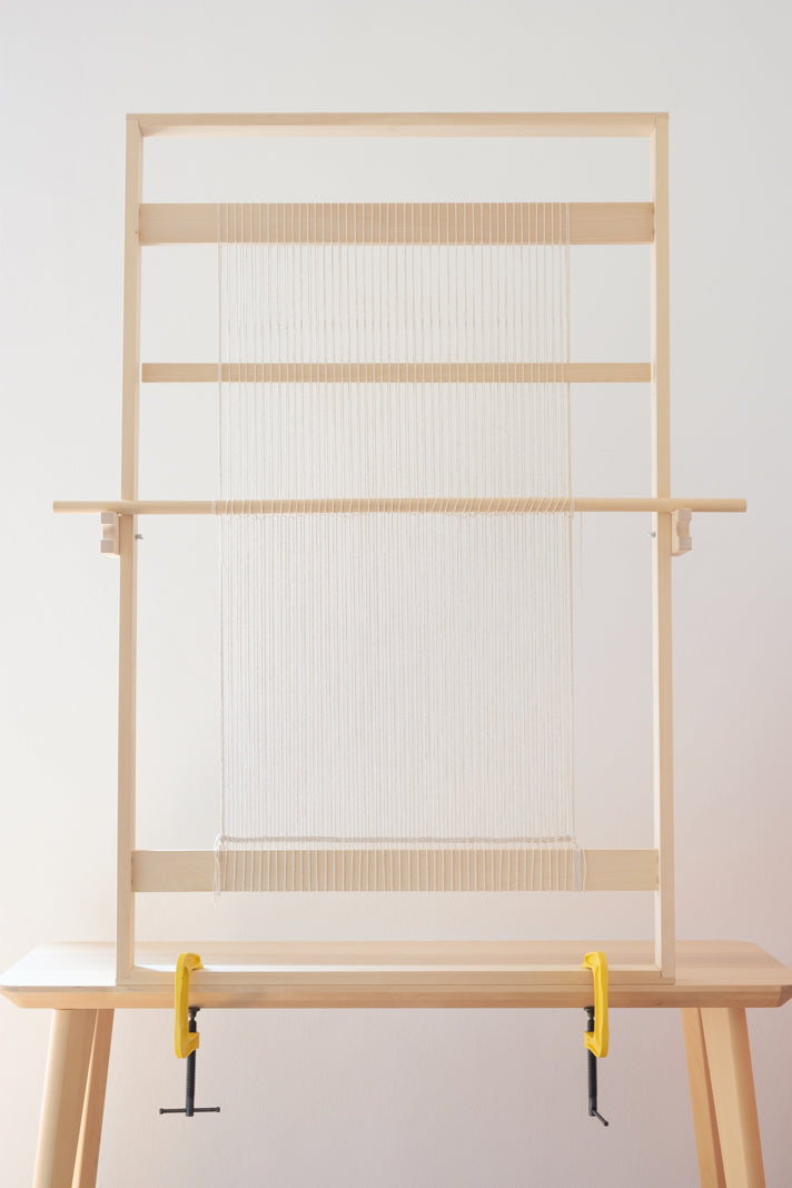 Telaio verticale in legno massello per tessitura di tappeti e arazzi, montato su un tavolo in legno, con orditura in cotone