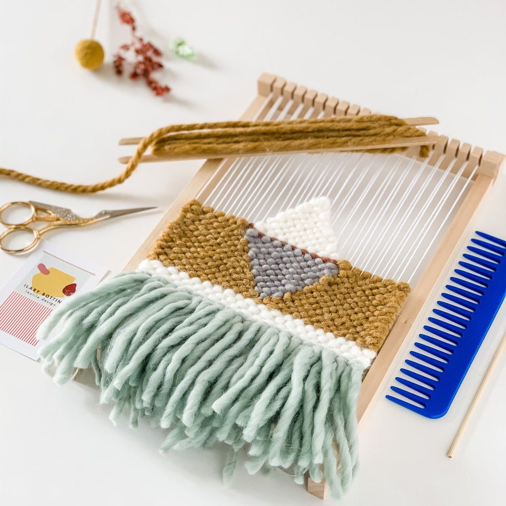 Piccola opera tessile parzialmente tessuta su un telaio a cornice, base senape con frange azzurre, accessori da tessitura 