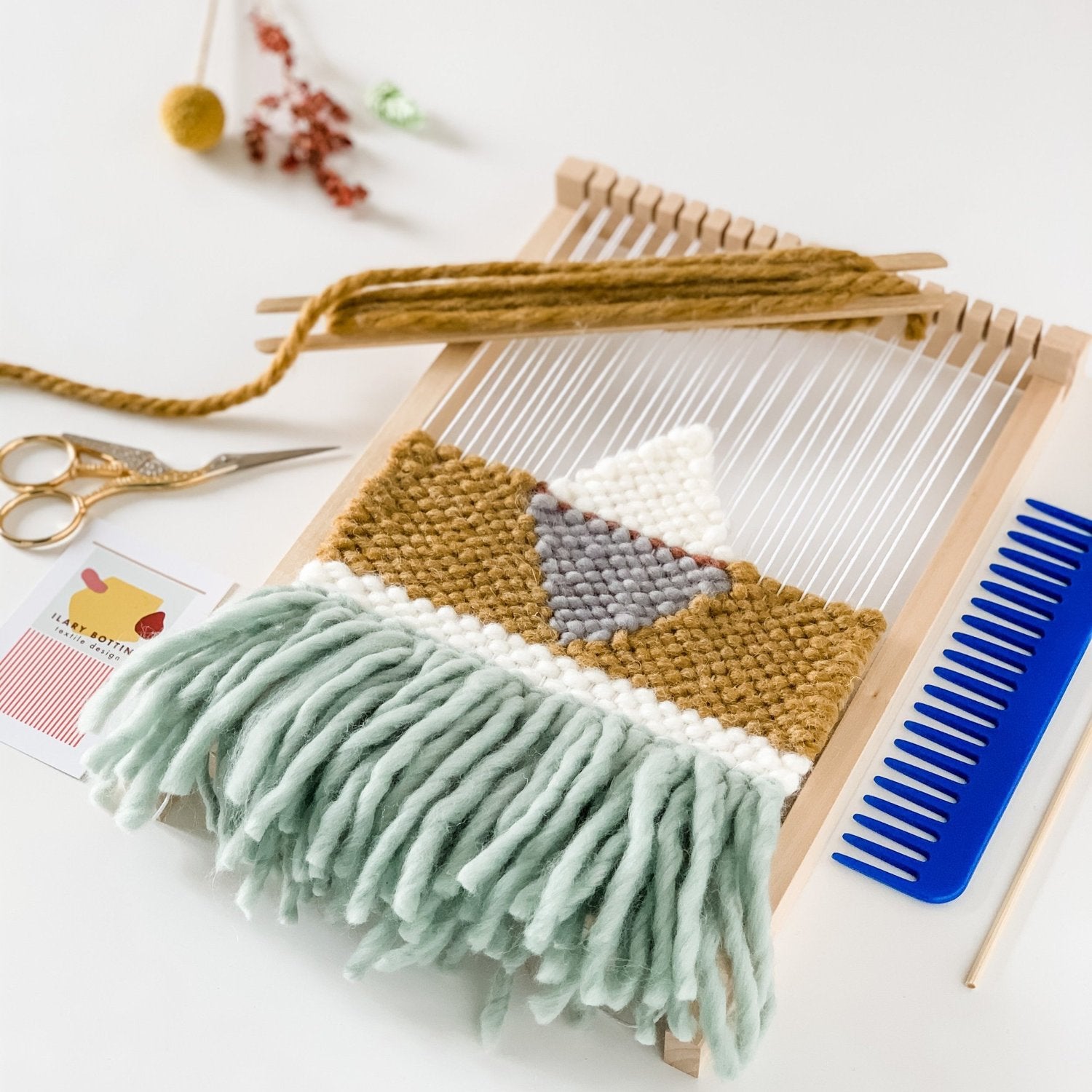 Piccola opera tessile parzialmente tessuta su un telaio a cornice, base senape con frange azzurre, accessori da tessitura 