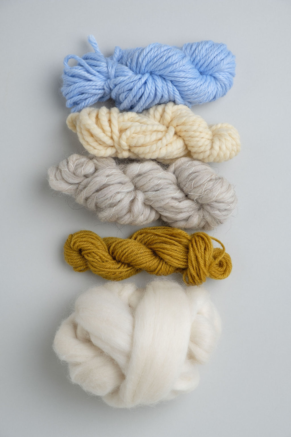 Gomitoli di lane da tessitura a telaio in colore azzurro, bianco, grigio e senape