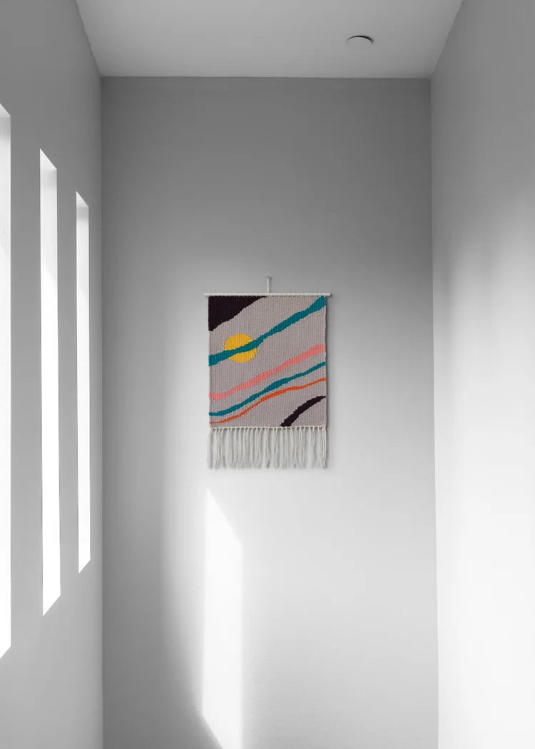 Arazzo contemporaneo in lana con base grigia, striature diagonali di colore arancione, rosa, verde e nero e cerchio giallo