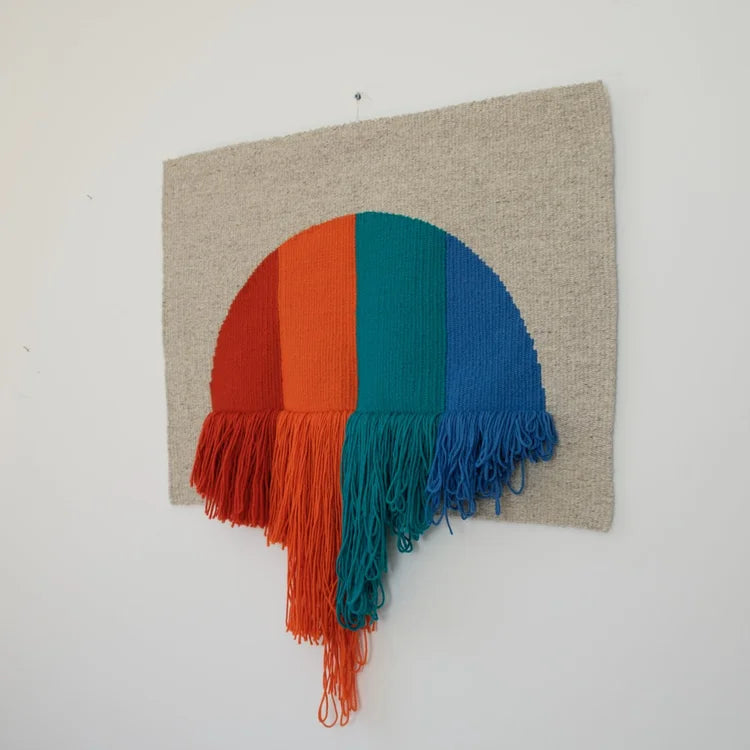 Arazzo contemporaneo in lana su base in cotone di Ilary Bottini con forma semicircolare e campiture verticali nei toni rosso, arancio, verde e blu, con frange decorative nella parte inferiore.
