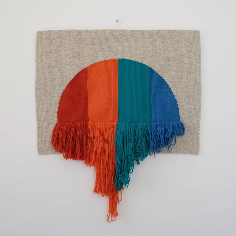Arazzo contemporaneo in lana su base in cotone di Ilary Bottini con forma semicircolare e campiture verticali nei toni rosso, arancio, verde e blu, con frange decorative nella parte inferiore.