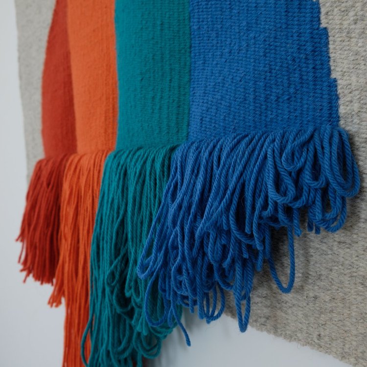 Arazzo contemporaneo in lana su base in cotone di Ilary Bottini con forma semicircolare e campiture verticali nei toni rosso, arancio, verde e blu, con frange decorative nella parte inferiore.